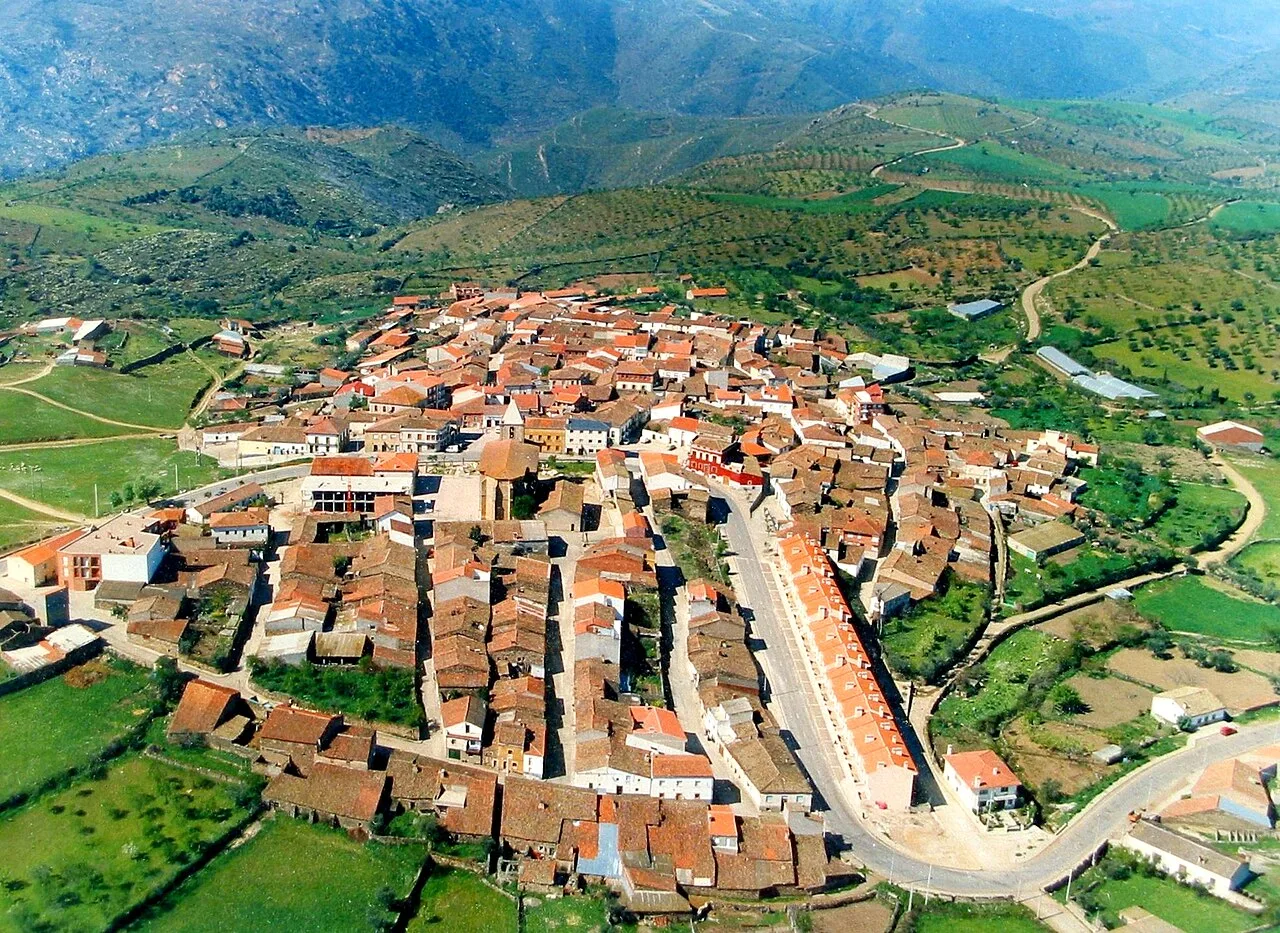 Vista aérea de un pueblo con calles estrechas y casas de tejado rojo en un entorno montañoso.