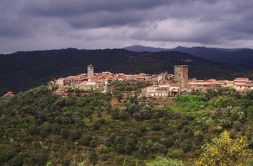 Vista panorámica de Miranda del Castañar con torres y casas antiguas en un paisaje montañoso.