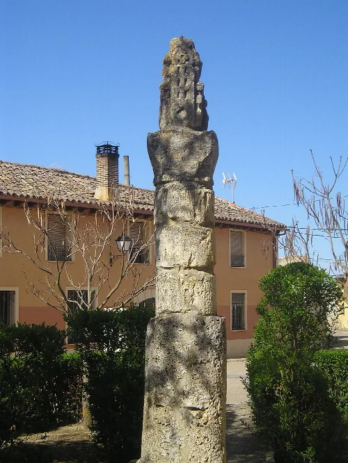Stone monument next to a church and trees in Santoyo