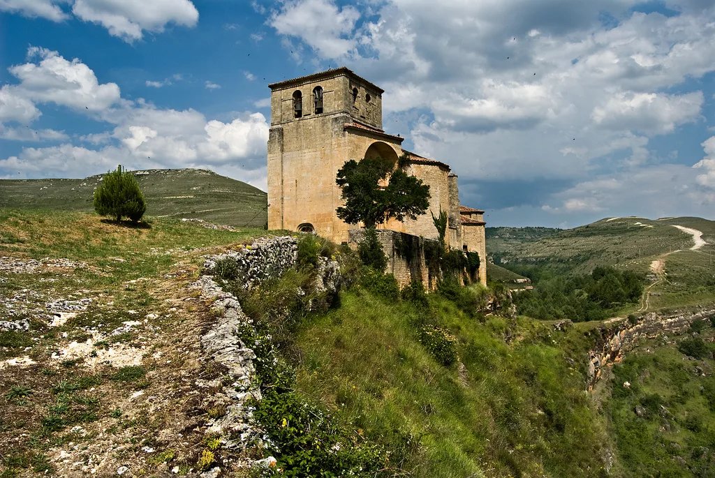 Alte Kirche in einer Landschaft mit Hügeln und ländlichen Wegen in Sedano.