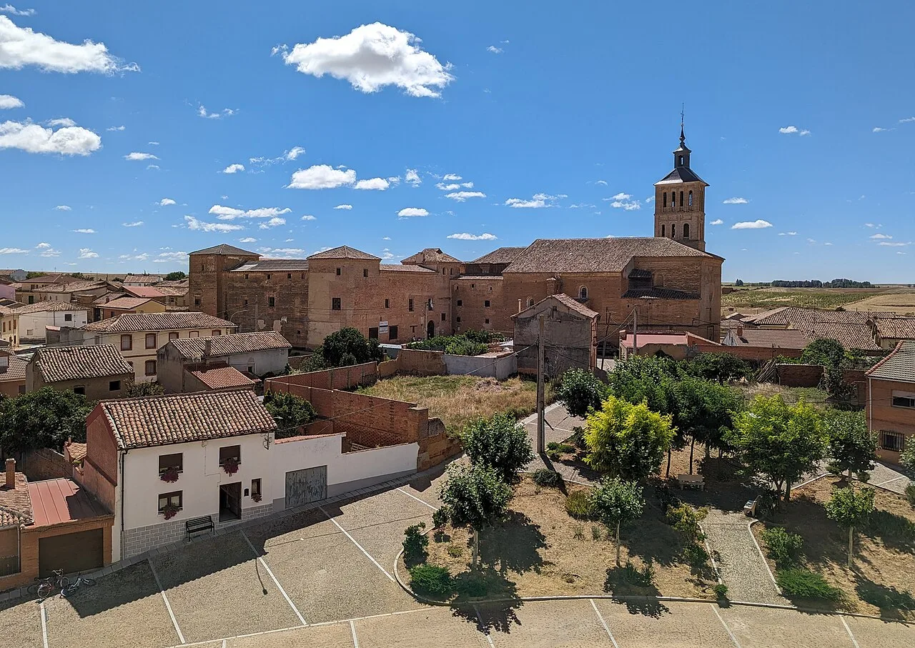 Panoramablick auf Grajal de Campos mit Kirche und Häusern unter blauem Himmel.