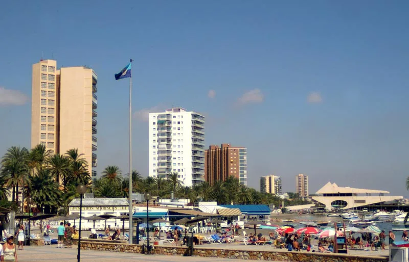 Hohe Gebäude, Palmen und Touristen am Strand von Santiago de la Ribera.