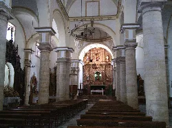 Interior of a church with columns, wooden benches, and an altar in the background.