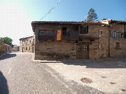 Casa de piedra con balcón y bandera española en Villardeciervos.
