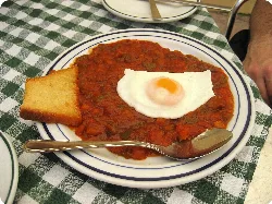Dish of pisto with egg and toast on a checkered tablecloth.
