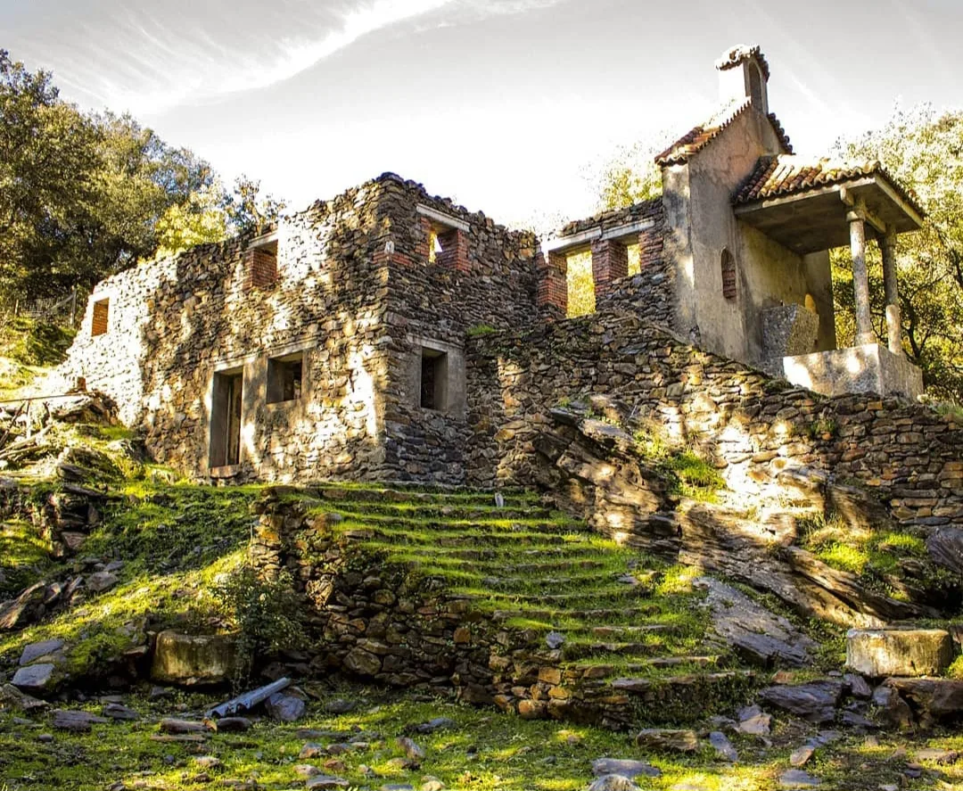 Ruinas de una ermita de piedra con escaleras y columnas en un entorno natural.