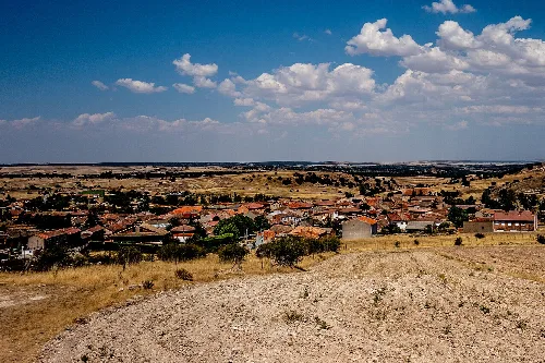 Panoramic view of Vegas de Matute with houses and fields under a sky with clouds.