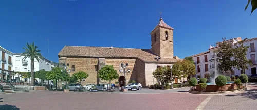 Steinige Kirche mit Turm und Platz mit Brunnen und Bäumen in Valdepeñas de Jaén.