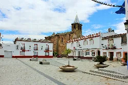 Main square with white buildings and a stone church in the background.