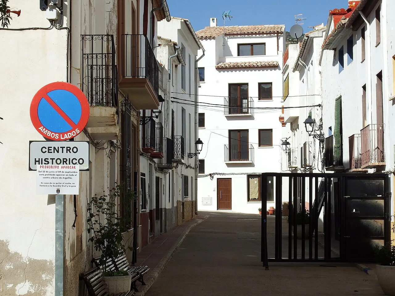 Calles blancas y estrechas en Argelita con cartel de no estacionar y banco.