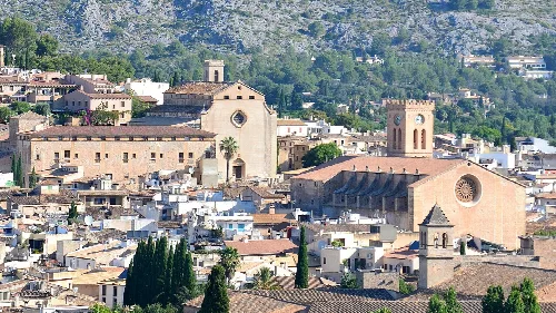 Dächer und Kirchen in Pollensa mit grünen Hügeln im Hintergrund