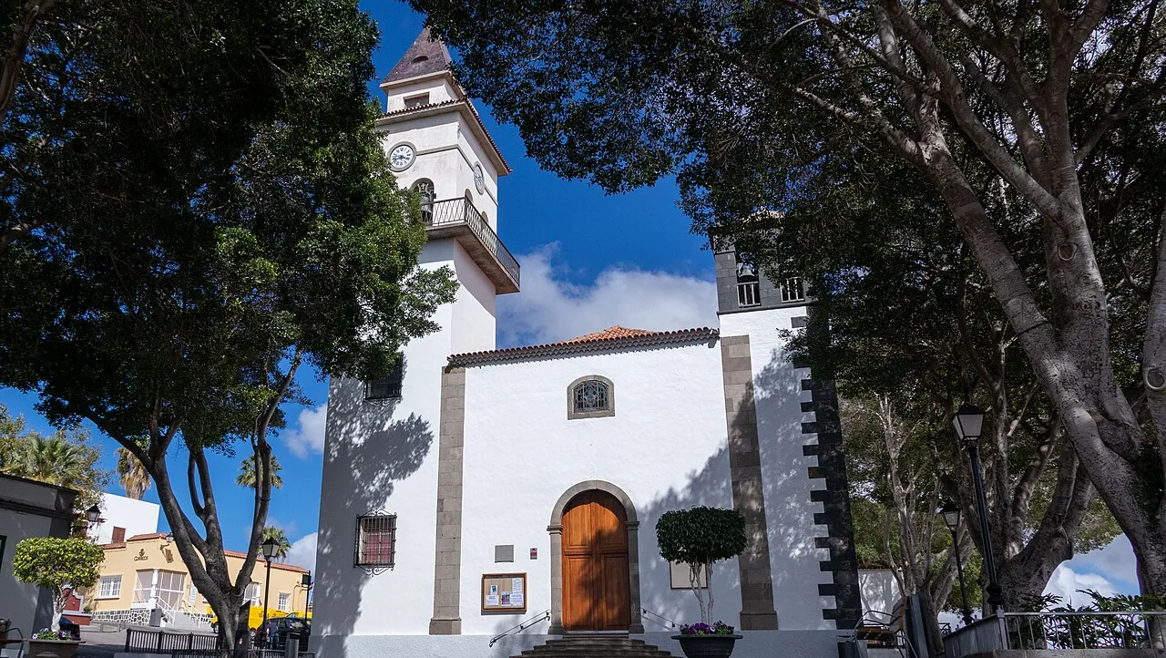 Facade of San Miguel Arcángel church with trees and blue sky.