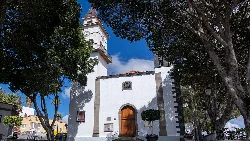 Facade of San Miguel Arcángel church with trees and blue sky.