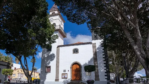 Facade of San Miguel Arcángel church with trees and blue sky.