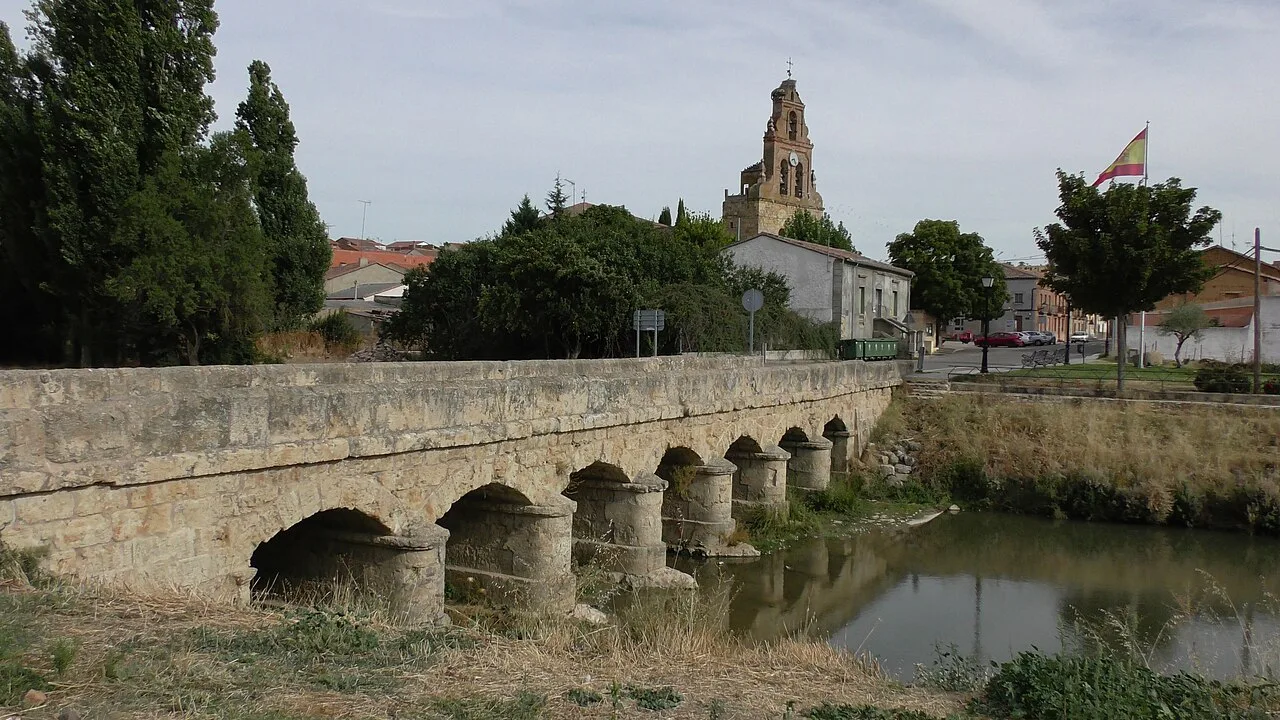 Stone bridge over a river with a church in the background in Venialbo.