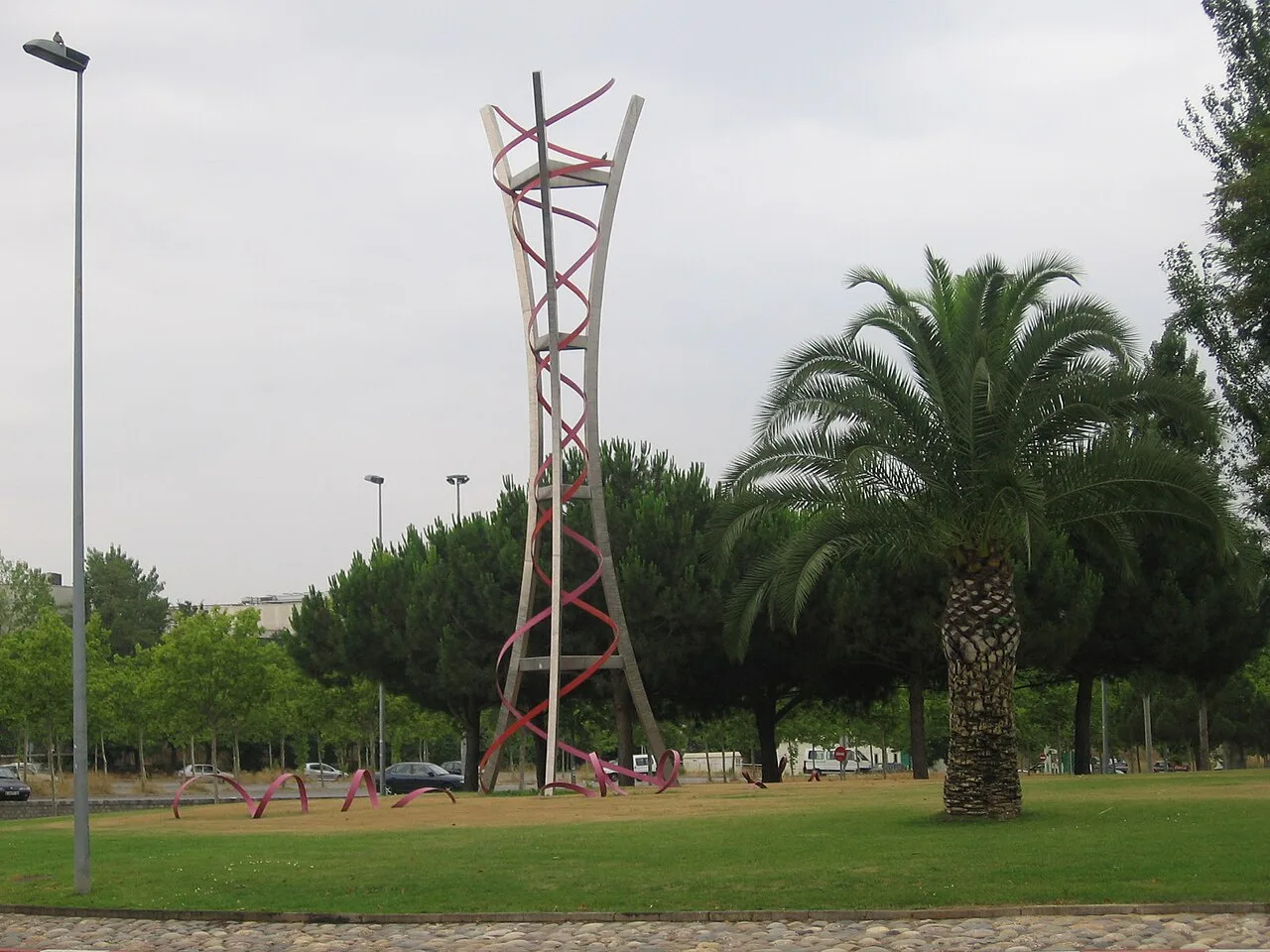 Kreisverkehr mit einer Metallskulptur in einem Park mit Palmen und Bäumen.