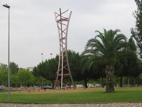 Kreisverkehr mit einer Metallskulptur in einem Park mit Palmen und Bäumen.