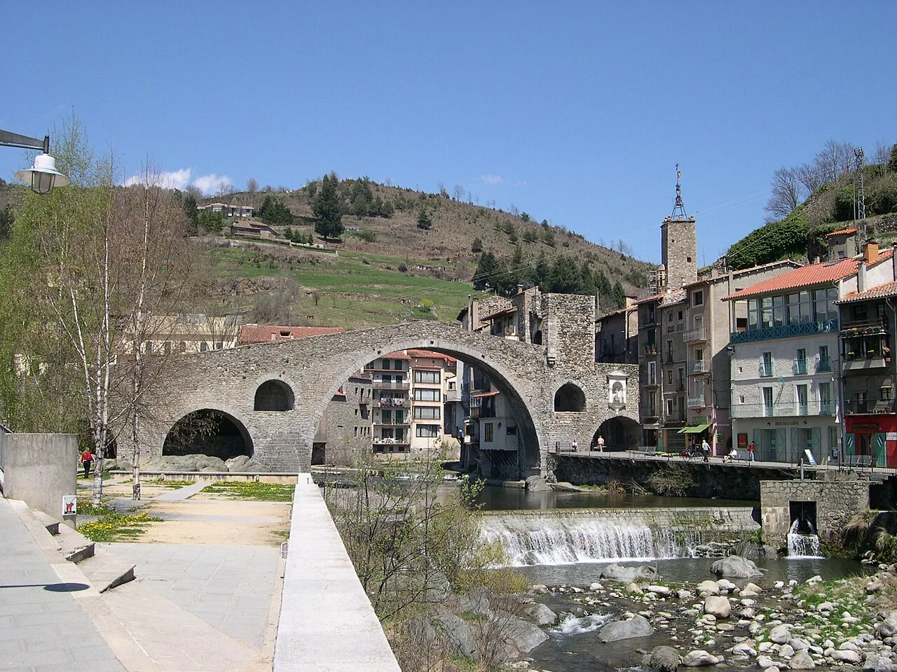 Puente de piedra con casas y montañas en el fondo.
