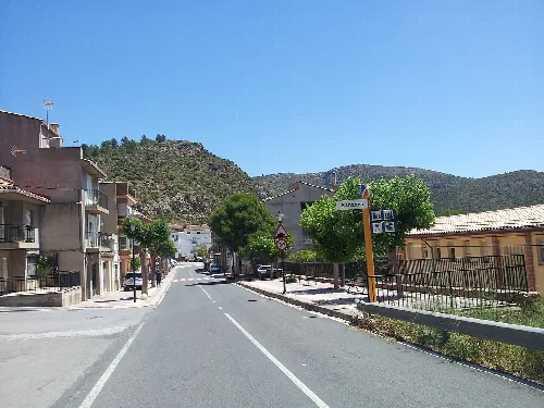 Calle de Fanzara con casas, árboles y señal de tráfico en un día soleado.