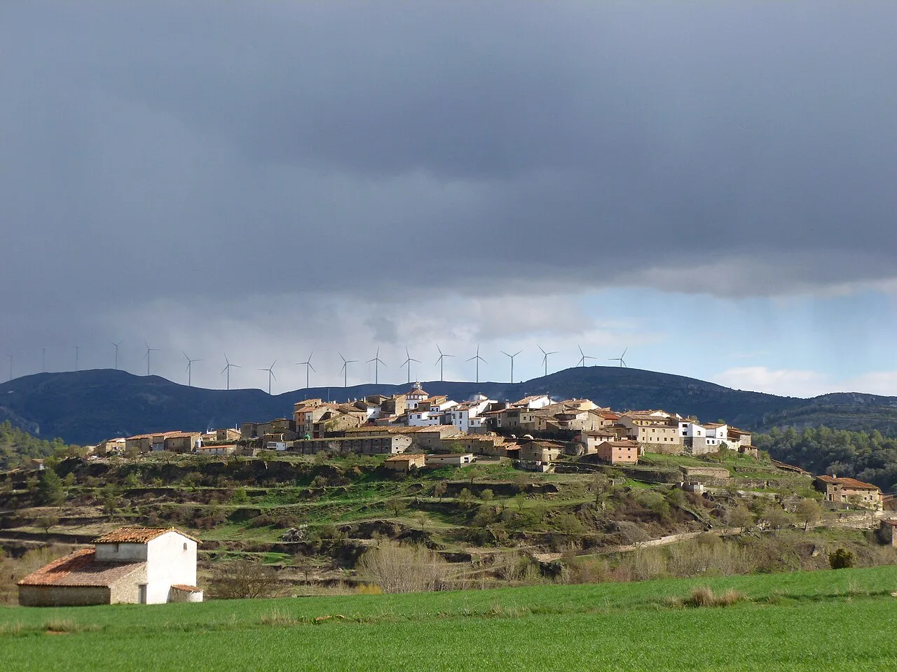 Pueblo en una colina con molinos de viento y río en el fondo.