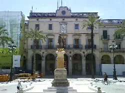 Town hall building with statue in the center and palm trees in the square.
