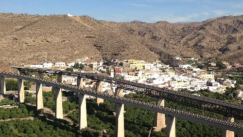 Vista de un castillo y una torre en Santa Fe de Mondújar, con pueblo y montañas.