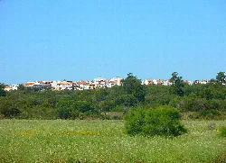 Paisaje con casas blancas en la colina y campo verde en primer plano.