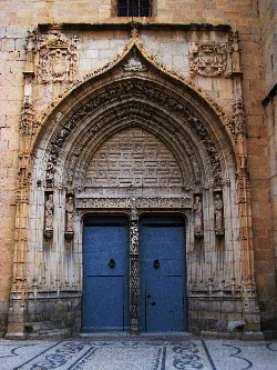 Kirchentür mit gotischem Bogen und Skulpturen am Eingang.