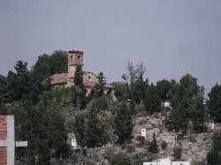 Fassade der San Antonio-Hermitage in Rugat, mit Bäumen und Gebäuden auf dem Hügel.