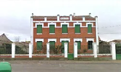 Edificio de dos plantas con fachada de ladrillo y ventanas verdes en Martín Muñoz de la Dehesa.