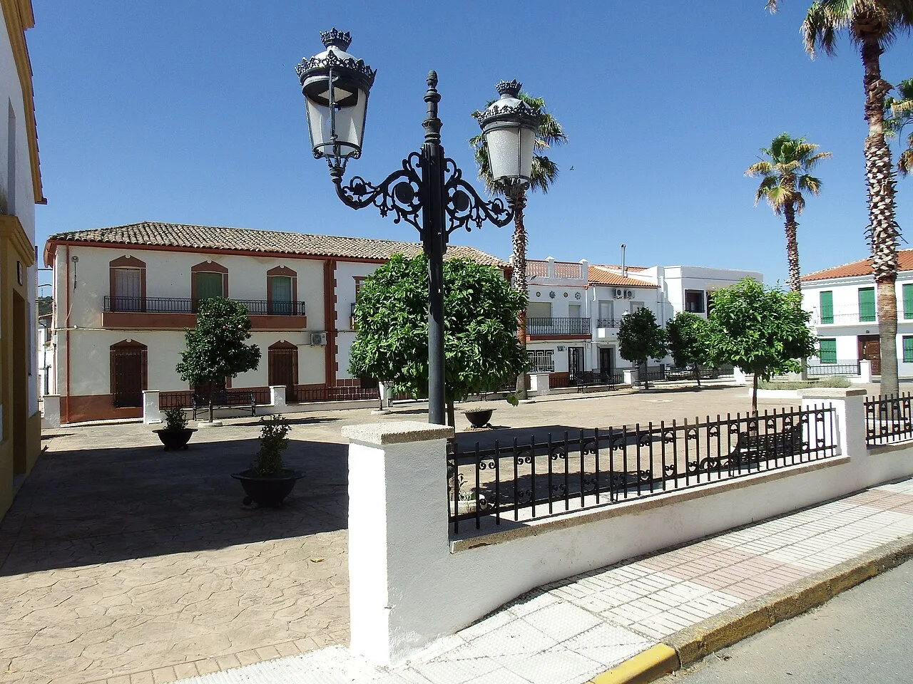 Square with an old lamp post, trees, and white buildings in Alamillo.