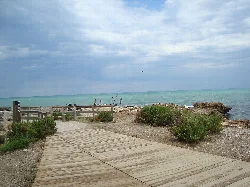 Wooden walkway and vegetation at Torrelasal beach with sea and cloudy sky.