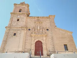 Facade of an old church with bell tower and wooden door in Gádor.