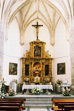 Main altar of the church with paintings, gold details, and white flowers.