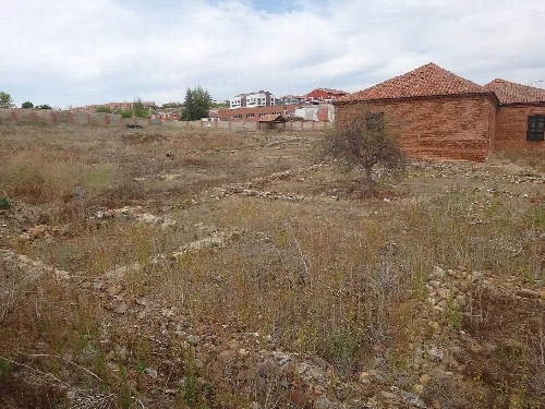Römische Ruinen auf einem Land mit Vegetation und modernen Gebäuden im Hintergrund.